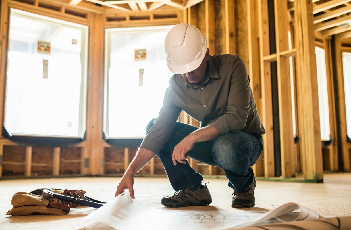 contractor wearing a hard hat inspecting blueprint on a floor atascadero ca